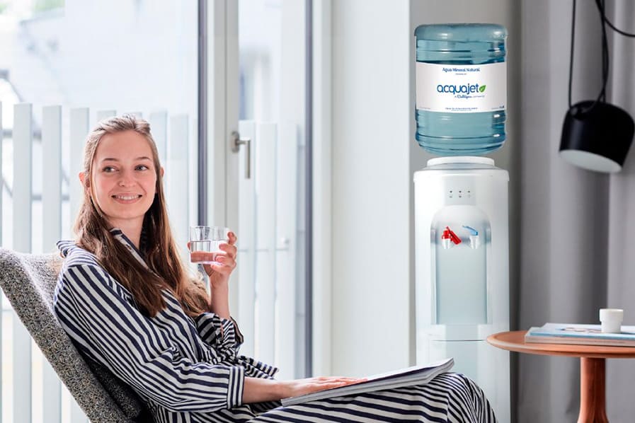 Dispensador de agua, mujer que toma agua fría en el vidrio del